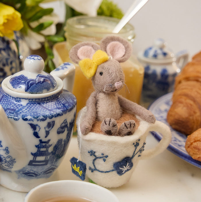 Hand-felted wool ornament of a small gray mouse with a bow, sitting inside a floral teacup with embroidered details. Crafted from merino-blend wool, this whimsical piece evokes tea time and childhood storytelling. Includes a hanging string and measures approximately 4.5 inches tall. A sweet and cozy decoration for tea lovers and mouse enthusiasts alike.