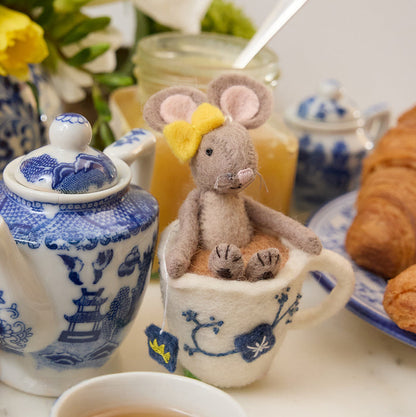 Hand-felted wool ornament of a small gray mouse with a bow, sitting inside a floral teacup with embroidered details. Crafted from merino-blend wool, this whimsical piece evokes tea time and childhood storytelling. Includes a hanging string and measures approximately 4.5 inches tall. A sweet and cozy decoration for tea lovers and mouse enthusiasts alike.