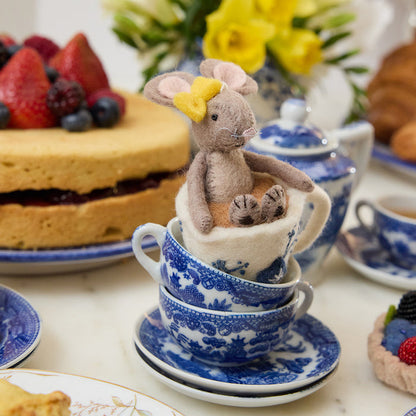 Hand-felted wool ornament of a small gray mouse with a bow, sitting inside a floral teacup with embroidered details. Crafted from merino-blend wool, this whimsical piece evokes tea time and childhood storytelling. Includes a hanging string and measures approximately 4.5 inches tall. A sweet and cozy decoration for tea lovers and mouse enthusiasts alike.