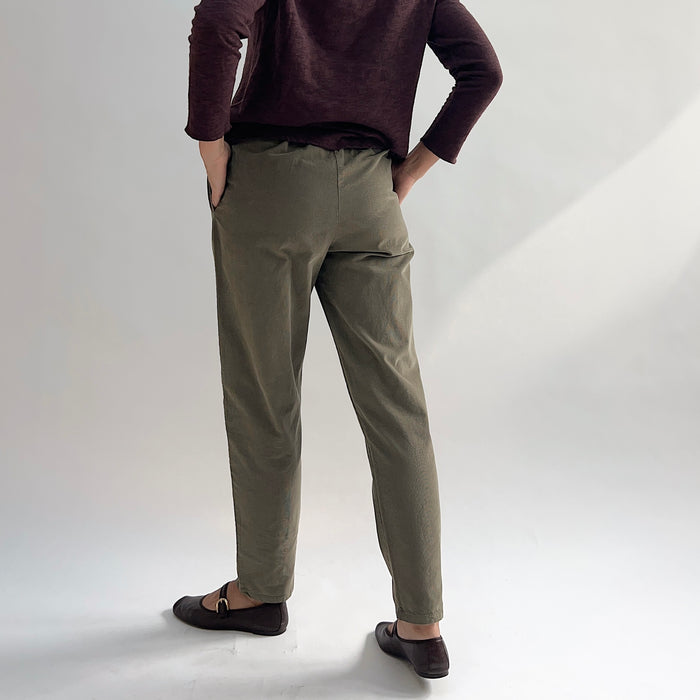 Back view of model wearing the Bryn Walker Corduroy Boslow Pants in Jasper, showing elastic waistband, relaxed tapered leg, ankle length, and olive jasper pinwheel corduroy, styled with burgundy Double Cotton Tee and brown Mary Jane flats