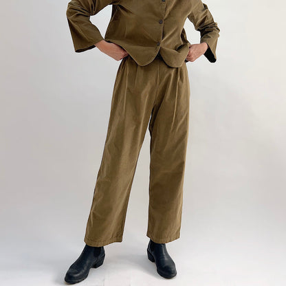 Model with hands on hips wearing the Bryn Walker Corduroy Pleated Pants in Partridge, front view showing front pleats, straight leg silhouette, and olive pinwheel corduroy, paired with matching Standing Collar Crop Jacket and black Chelsea boots