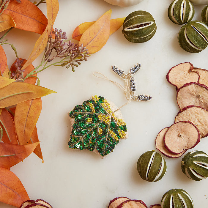 Fall-themed beaded maple leaf ornament featuring intricate beadwork and hanging seed pod charms, handcrafted in India.