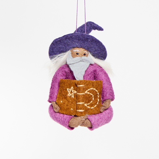 Hand-felted wool ornament of a grey-bearded wizard wearing a pointed hat, holding an open spell-book beneath swirling stardust. Featuring a warm-toned complexion, white hair, and flowing robes, this whimsical figure is crafted from natural merino-blend wool. Includes a hanging string and measures approximately 5 inches tall. GIF 360 degree view.