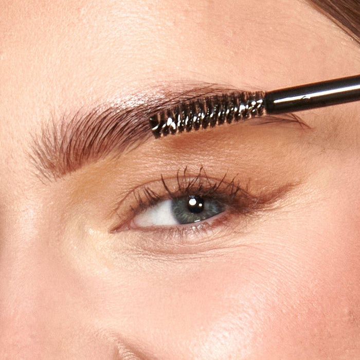 A close up of models eyebrow with the brush applying the product.