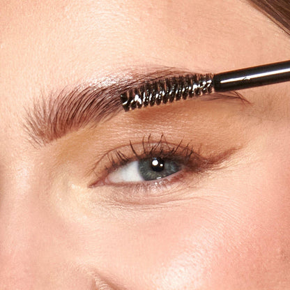 A close up of models eyebrow with the brush applying the product.