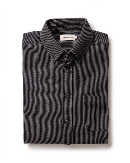 The Jack in Roped Black Indigo by Taylor Stitch, folded flat lay showing roped indigo stripe texture, button-down collar, and chest pocket with Taylor Stitch label